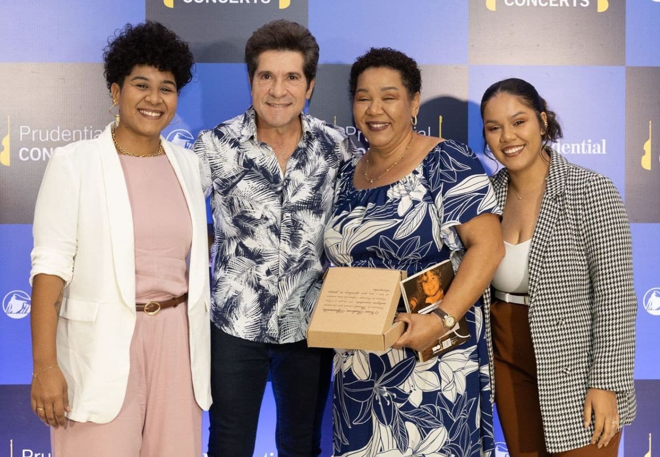 Mulher segura rosa vermelha e papel autografado próximo a um palco iluminado.