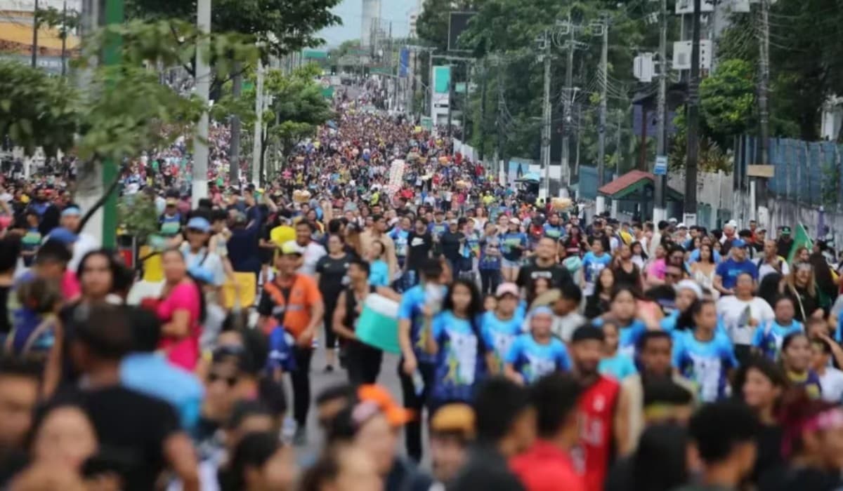 Multidão caminha em avenida de Manaus durante evento religioso com faixas coloridas.