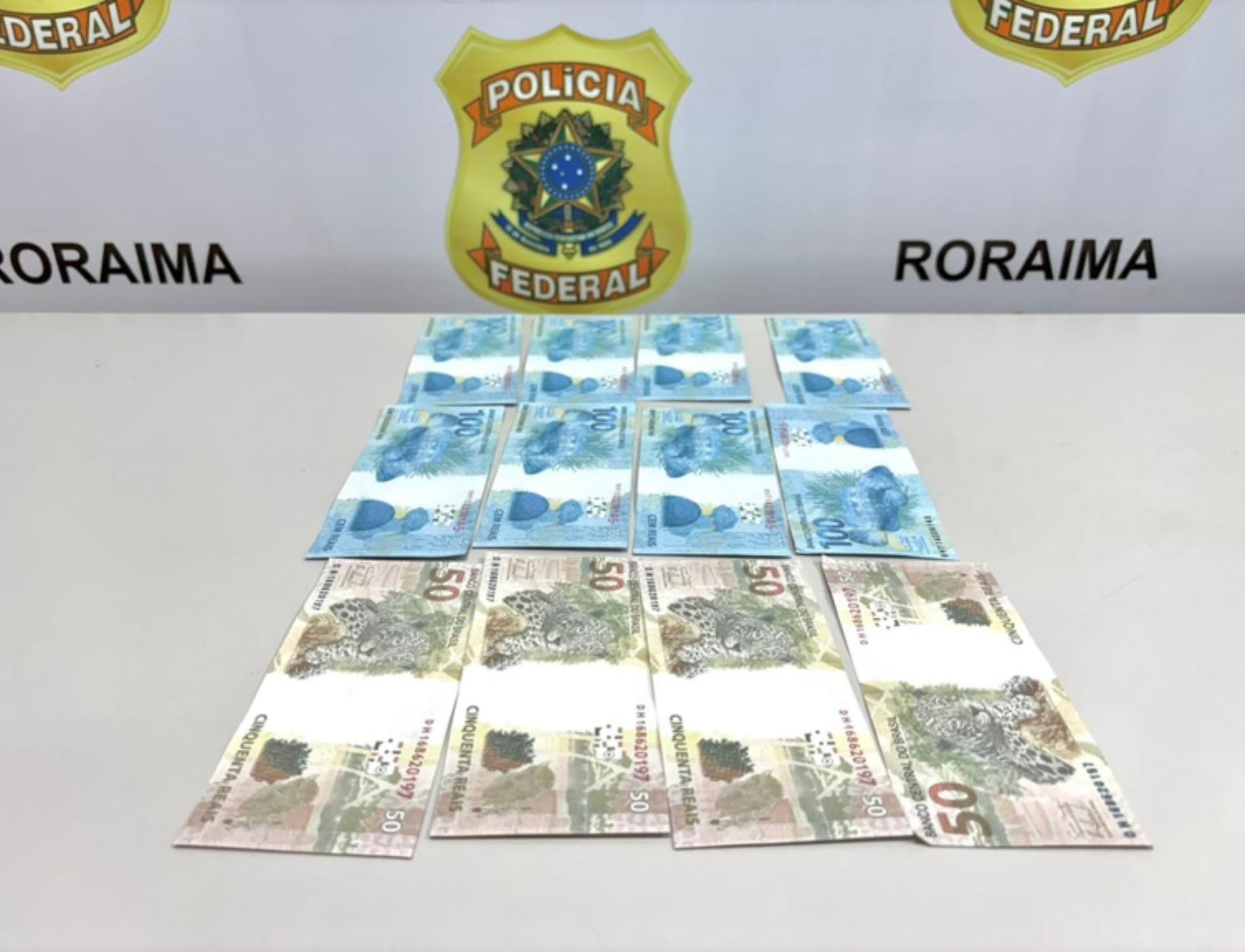 Cédulas de real apreendidas pela Polícia Federal sobre superfície lisa durante operação em Roraima.