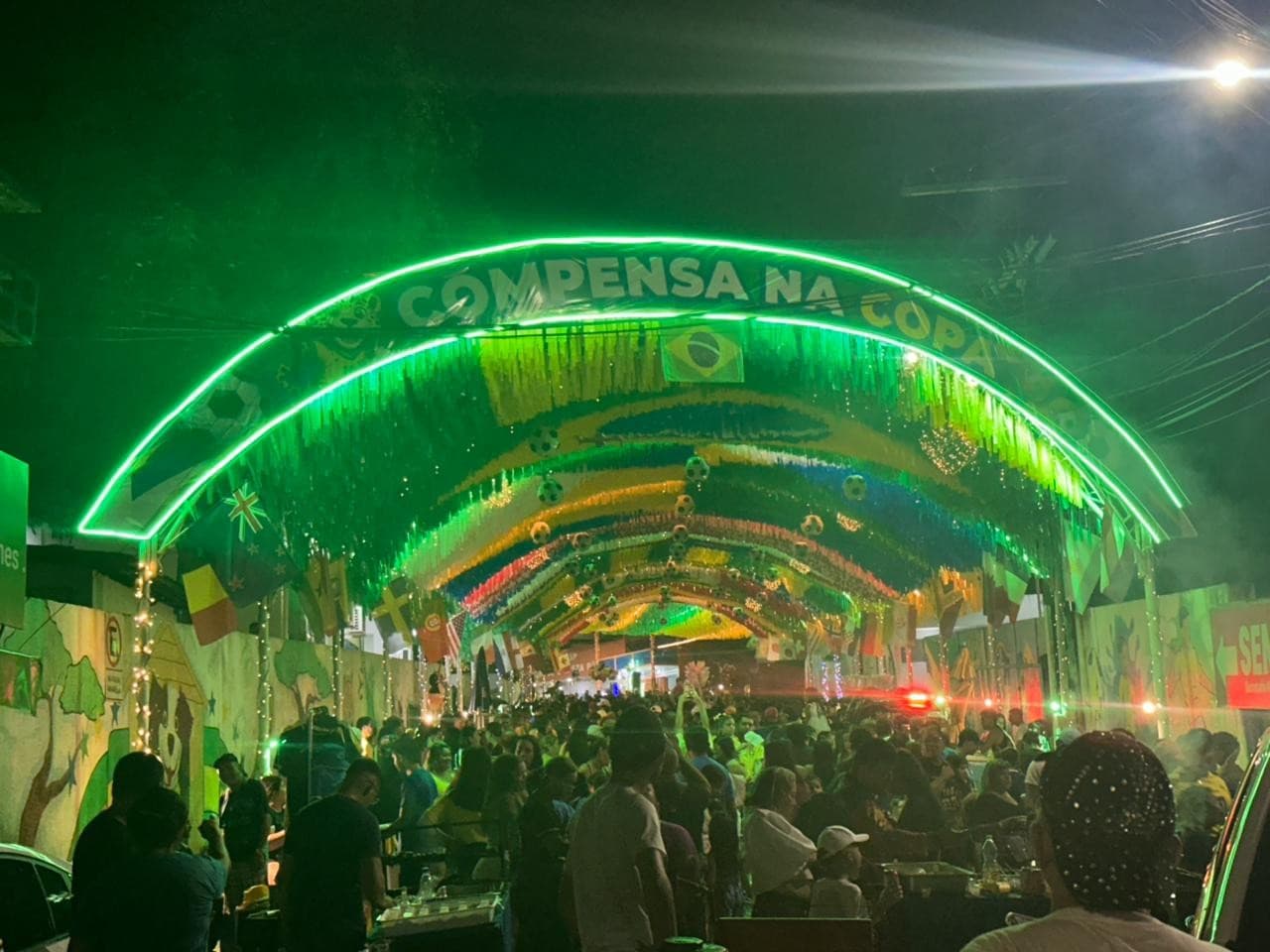 Rua iluminada com decoração colorida feita de garrafas pet e painéis reciclados durante festa no bairro Compensa.