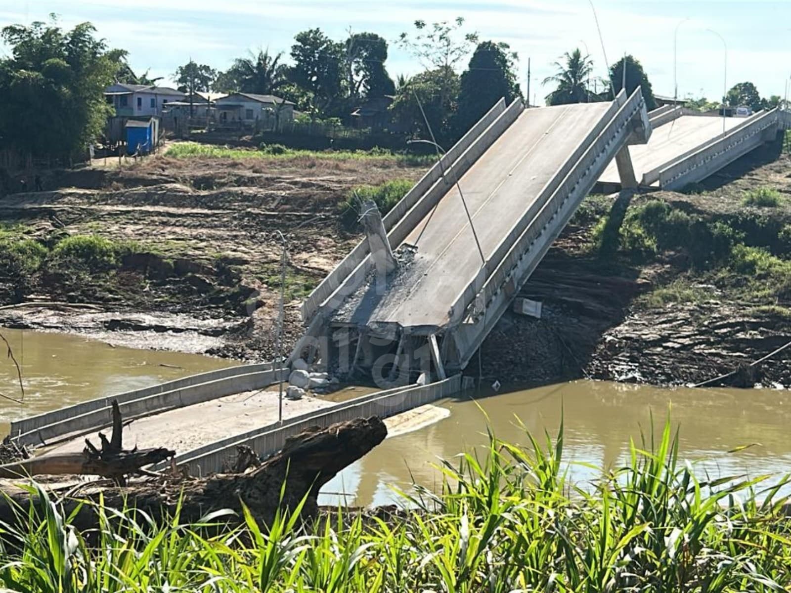 Estrutura destruída da ponte sobre o Rio Iaco em Sena Madureira, com detritos na margem.