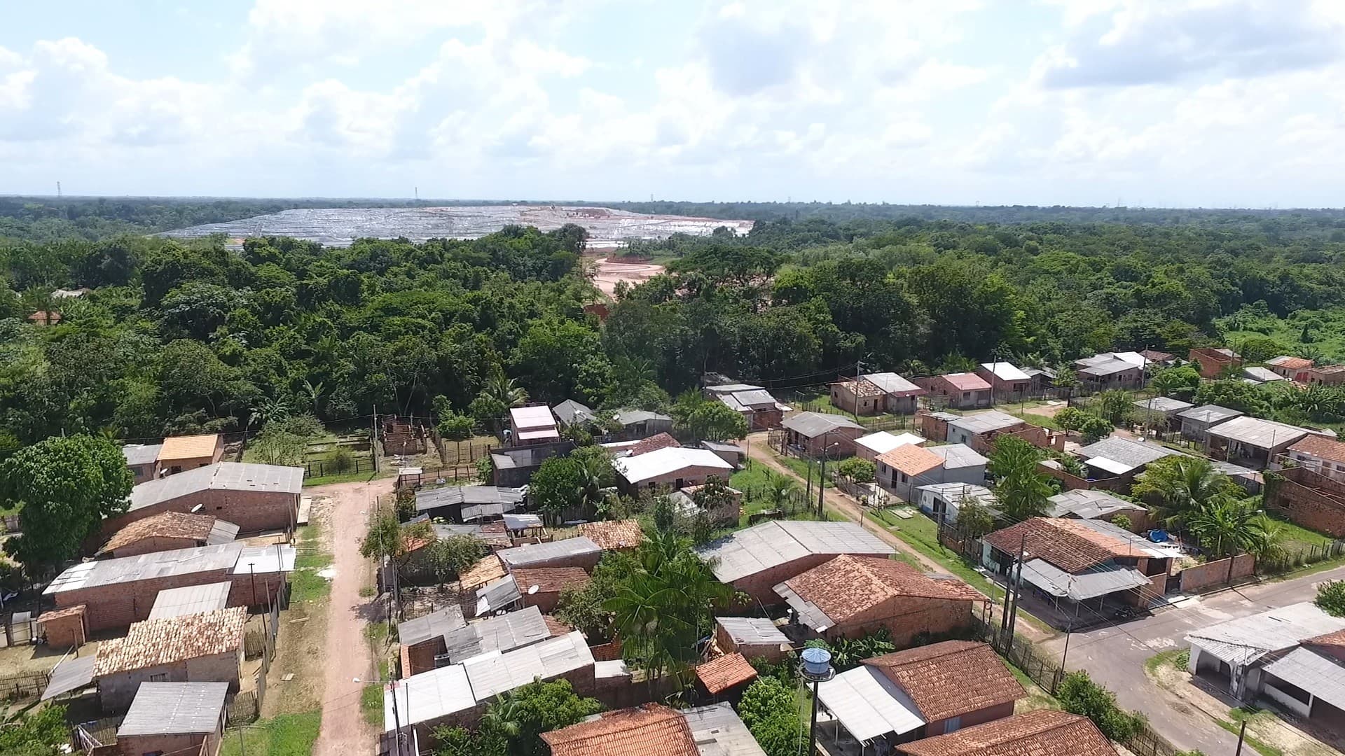 Caminhão de lixo sobe rampa do Aterro Sanitário de Marituba, ao fundo residências próximas.