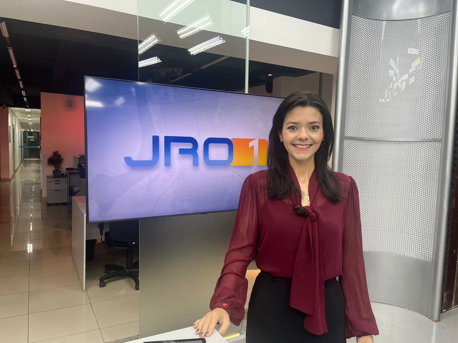 Mulher idosa assiste telejornal em sala iluminada por lâmpada durante tarde de chuva forte.