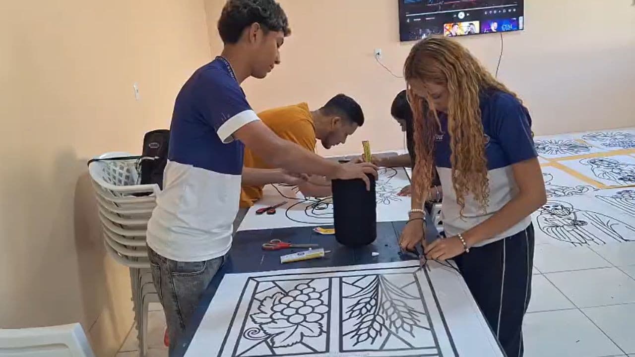 Mãos tingidas espalham serragem colorida formando desenho religioso em calçamento de igreja.