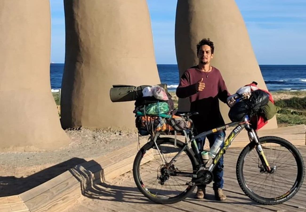 Ciclista empurra bicicleta carregada com bagagens em estrada de terra ao entardecer.